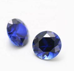 two blue sapphires on a white surface, one is round and the other is oval