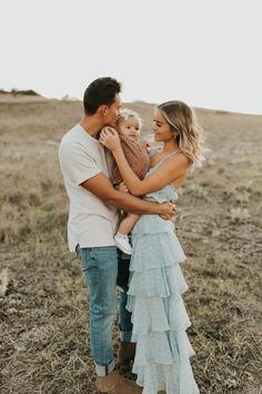 a man and woman are holding their baby in the middle of an open field with grass