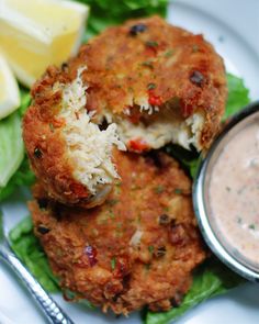 two crab cakes are on a plate with lettuce and sauce next to it