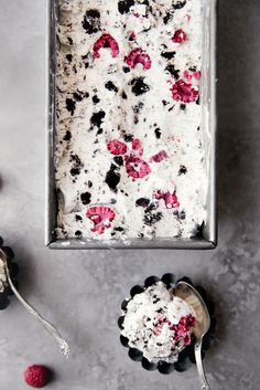 a pan filled with ice cream and raspberries on top of a counter next to two spoons