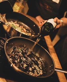 a person pouring wine into a skillet filled with mussels and other food