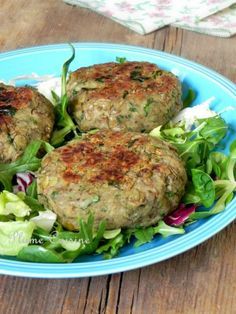 three meat patties on top of lettuce and salad in a blue bowl