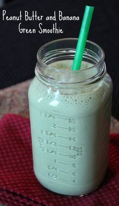 a mason jar filled with green smoothie on top of a red towel next to a spoon