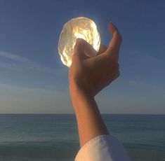 a person holding up a crystal ball in front of the ocean on a sunny day