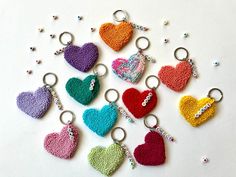 six crocheted heart shaped keychains are arranged on a white surface with beads and sequins