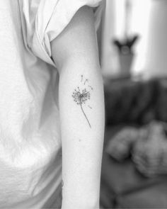 a black and white photo of a woman's arm with a dandelion tattoo