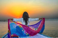 a woman sitting on the back of a boat holding a colorful scarf over her shoulder