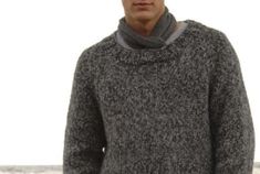 a man standing in front of the ocean wearing a gray sweater