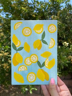 a hand holding up a piece of paper with lemons and leaves painted on it