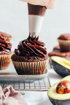 someone cutting into a chocolate cupcake with an avocado on the other side