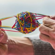 two hands are holding a ball of colored string and pulling it with one hand to the other