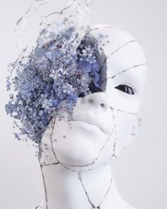 a white mannequin head with blue and purple flowers in it's hair