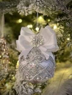 a christmas ornament hanging from a tree with white ribbon and bow on it