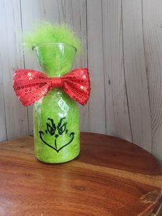 a green vase with a red bow on it sitting on a wooden table next to a white wall