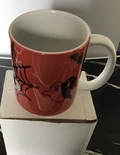 a red coffee cup sitting on top of a white box with a black cat drawn on it