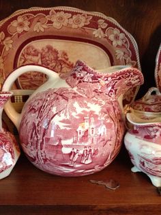 a red and white pitcher sitting on top of a wooden shelf next to other dishes