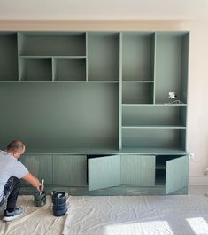 a man is painting the walls in a room with green shelving and white sheets