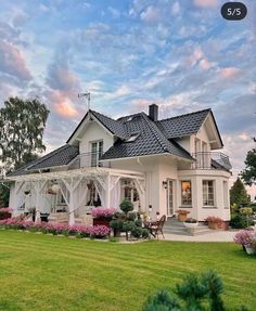 a large white house sitting in the middle of a lush green field with lots of flowers