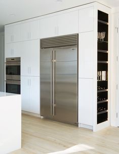 a stainless steel refrigerator in a kitchen with white cabinets and wood flooring on the walls