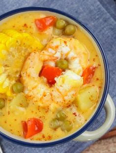 a bowl of soup with shrimp, carrots and green olives next to a spoon