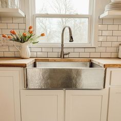 a kitchen sink sitting under a window next to a counter top with flowers in it