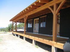 the front porch of a black cabin with wooden posts and wood slats on it