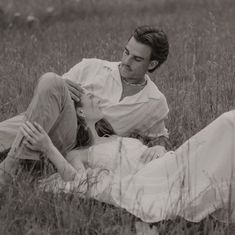 a man and woman laying on the ground in tall grass