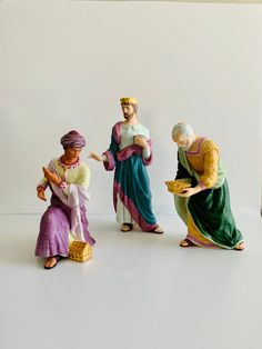 three figurines of people sitting on the ground and one is holding a bowl