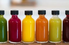 six bottles filled with different colored liquids on top of a wooden table