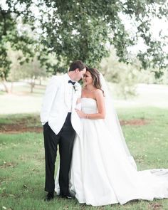 a bride and groom standing in the grass under a tree