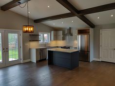 an empty kitchen and living room with wood floors, white walls, and wooden beams