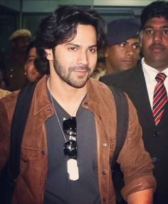 a man in a brown jacket and tie is walking with other men behind him, all looking at the camera