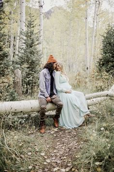 a pregnant couple sitting on a log in the woods