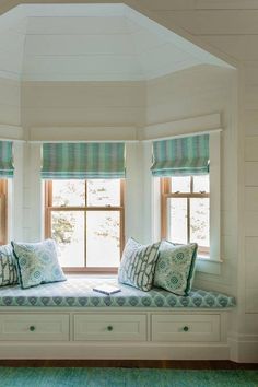 a window seat with pillows on it in front of two windows and a green rug