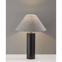 a black table lamp with a white shade on the base and a grey wall behind it