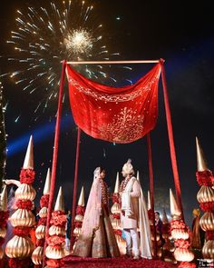 two people standing in front of a red and gold stage set with fireworks behind them