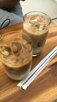 two glasses of iced coffee sitting on top of a wooden table next to chopsticks