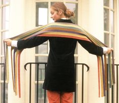 a woman is standing with her hands on her hips and holding a multicolored shawl over her shoulders