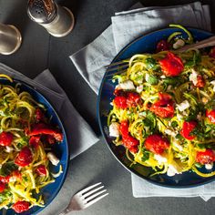 two plates of pasta with tomatoes, cheese and spinach on the table next to silverware