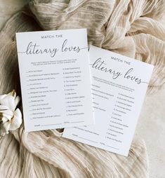 two white cards sitting on top of a bed next to a flower and a blanket