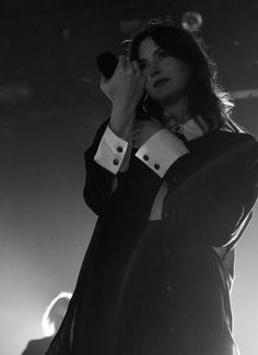 a man in a tuxedo holding a microphone up to his ear while standing on stage