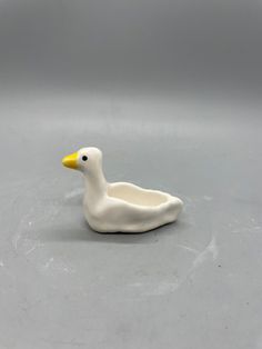 a white ceramic duck sitting on top of a gray floor next to a black and yellow object