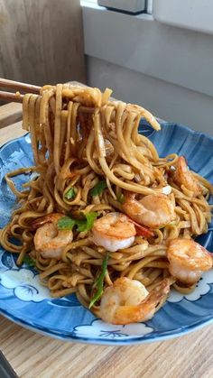 a blue plate topped with noodles and shrimp next to chopsticks on top of a wooden table