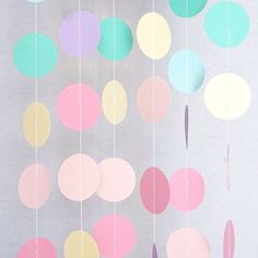 some paper circles hanging from strings on a gray background with pink, yellow and blue colors