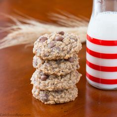 three oatmeal chocolate chip cookies next to a glass of milk on a table