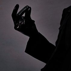 a person in a black suit holding an object up to their face with both hands