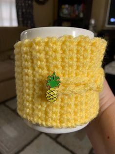 a yellow knitted cup holder with a pineapple pin on it