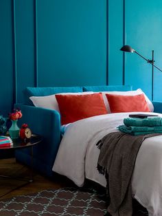 a bedroom with blue walls, white bedding and red pillows on the headboard