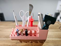 a pink pen holder with scissors, pens and other office supplies in it on a wooden table