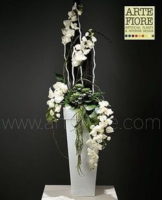 a white vase with flowers and greenery in it sitting on a pedestal against a black wall